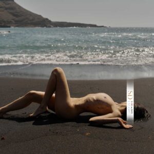 Foto einer zierlichen jungen Dame, die am Strand auf dem Rücken liegt und verführerisch posiert. Sie schaut Richtung Meer.